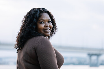 Closeup portrait of curly smiling african afro american dark skin woman looking at camera, posing against blue sky. Interracial, mixed race female model. Different skin ethnicity female. Copy space