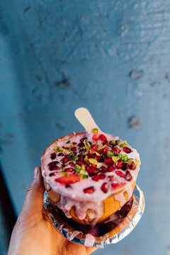 Woman holds bowl of pink lassi with pomegranite against blue wall