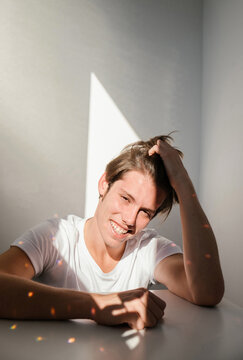 
portrait of a charming guy with long hair who smiles and falls on his face and T-shirt on a light background