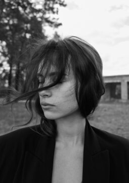 black and white portrait of a girl dressed in a black jacket with wavy hair that flutters in windy weather while walking through the forest