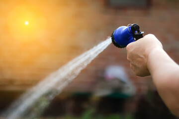 Defocus hand water garden. Female hand holding blue automatic sprinkler sprays water over brown...