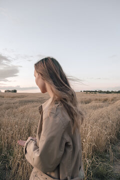 girl with long blonde hair in a tan coat while walking on a sunny field