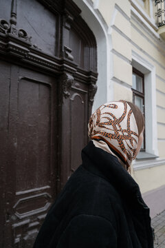 girl with a scarf on her head and in a black jacket on the background of an old building while walking around the city