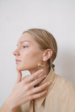 portrait of a girl in profile with a hand near her face and a flower in her, dressed in a beige shirt on a light background