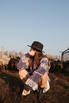 girl squatting on a background of a herd of sheep in a field on a farm