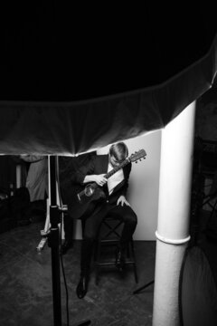 black and white photo of a musician guy getting up from a chair, holding a guitar in his hands