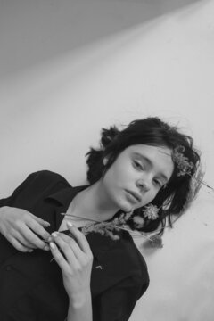 black and white portrait of a young girl lying on the floor in the studio in a dark shirt with flowers in her hair