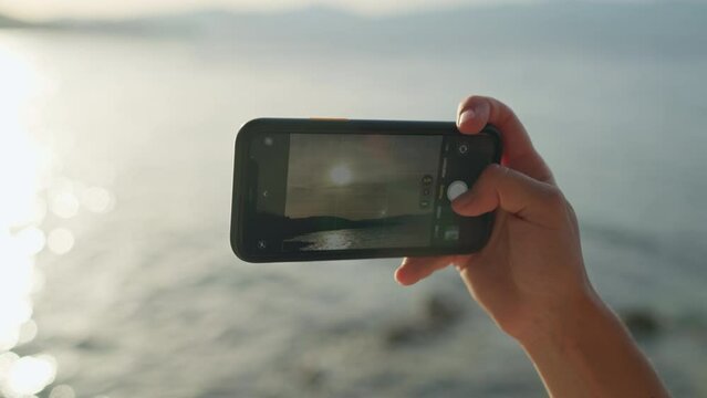 Close-up of a phone in female hands making a photo at sunset by the sea. Happy moments of life.