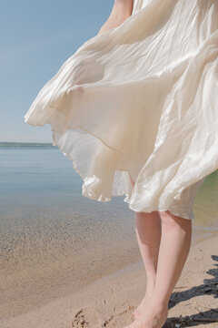 phot of a girl in a white dress flying in the wind while walking along the lake