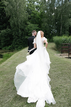 the bride and groom on a wedding walk, while walking, the airy dress of the bride with a long train flies