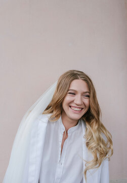 portrait of a laughing bride in a veil and white shirt on a light background