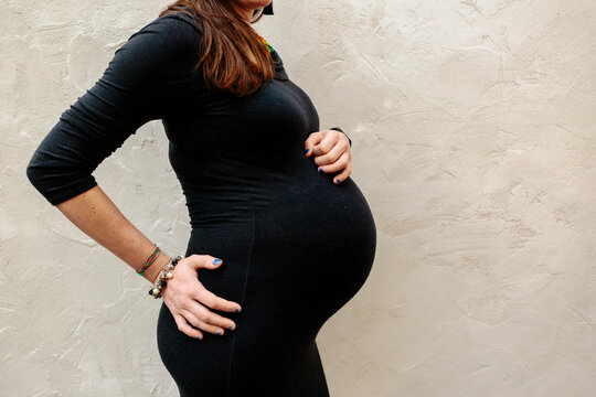 Body of advanced pregnant woman in black tight dress on profile 