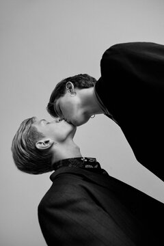 black and white portrait in which two guys in love in stylish clothes kiss each other