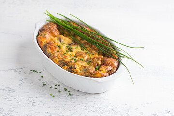 Casserole or clafoutis with mushrooms and cheese in a white ceramic baking dish sprinkled with green onions on a light background