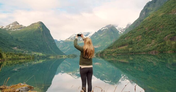 4k video footage of an unrecognisable woman standing and using her cellphone to photograph the lake in Stryn