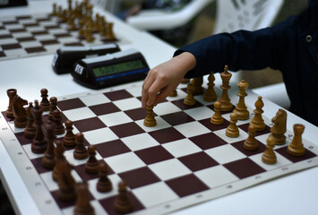 On a chessboard with a clock, a child's hand makes the first move with a pawn.