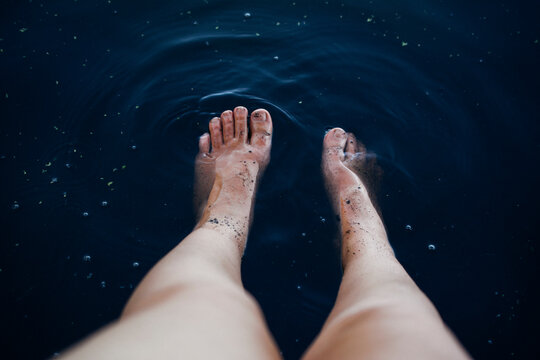 Adults' feet against dark pond water