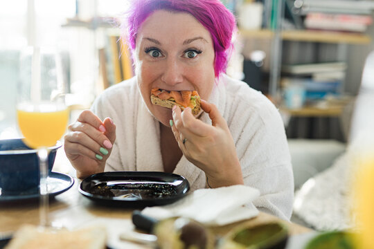 Woman with bright pink hair having breakfast grimacing to camera