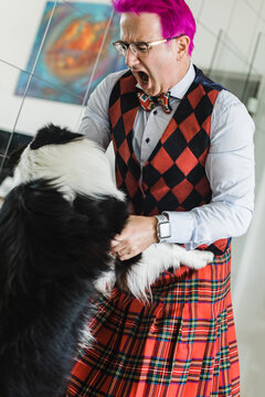 eccentric man with bright pink hair playing with a dog at home