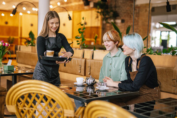 Female waiter providing service for visitors in cafe 