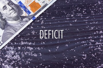 DEFICIT - word (text) on a dark wooden background, money, dollars and snow. Business concept (copy space).