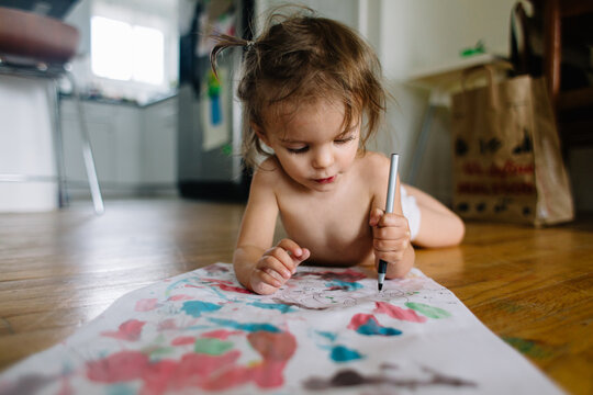 toddler draws picture while laying on the floor