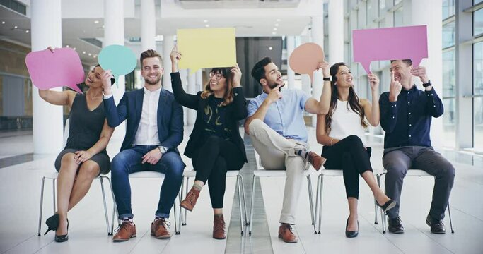 4k video footage of a group of confident young businesspeople seated next to each other while holding up speech bubbles inside of the office