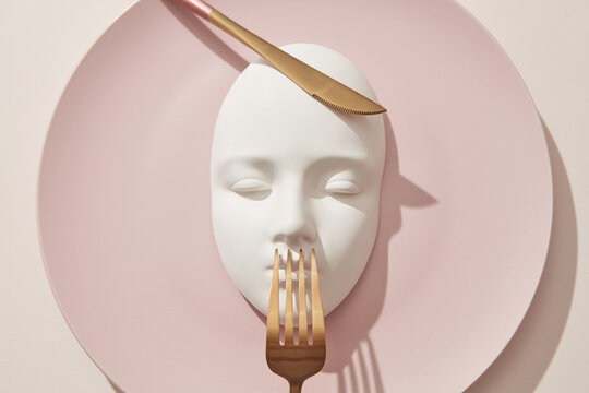 Plaster white mask served on pink plate with golden cultery