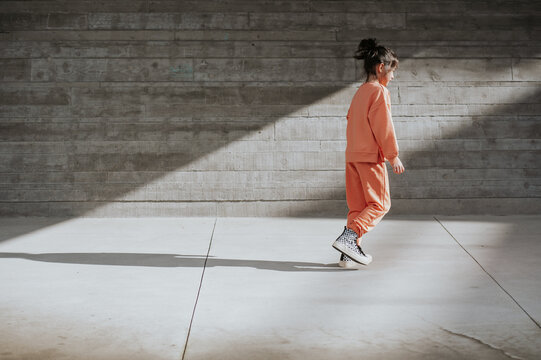 Young girl in workout clothes walks near a concrete wall in the sun.