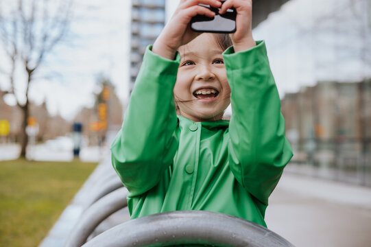 Young girl in a green raincoat takes a selfie with her phone.
