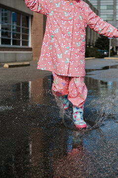 Young girl walks in a puddle with rain boots and an umbrella.