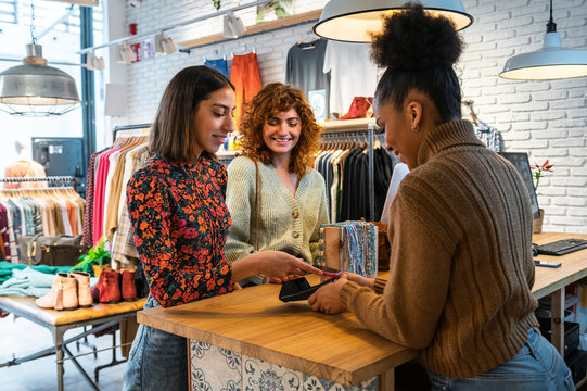 Diverse women paying phone in clothes shop