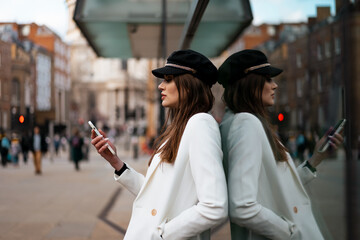 Woman leaning on a glass of a building and using a smartphone