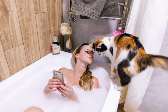 Female resting in bathtub with phone in hands and cat