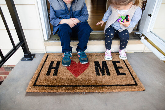 Children sitting on front porch of home with welcome mat