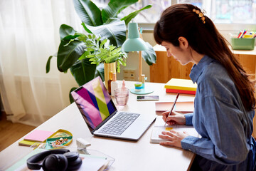 Woman writing in notepad while working on laptop