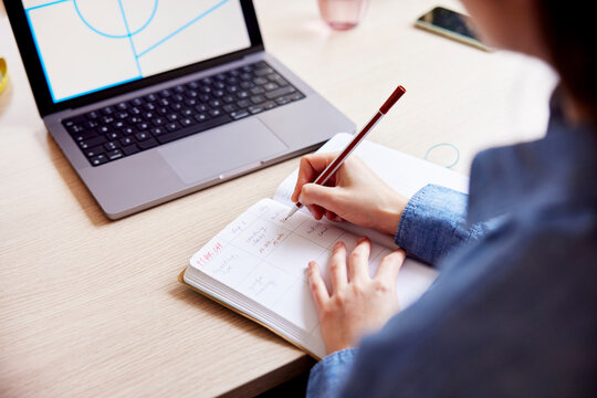 Woman writing in notepad while studying on laptop
