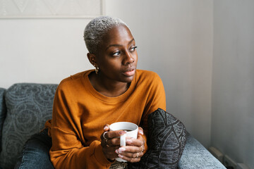 Curious woman drinking coffee on sofa