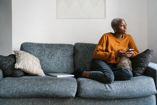 Thoughtful woman using smartphone on sofa