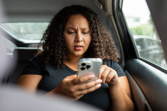 Woman Looks Concerned While Using Smart Phone In Backseat Of Car