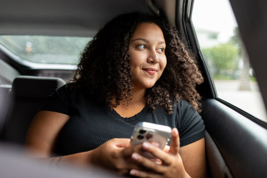 Young Woman Looks Out Car Window While Using Her Smartphone
