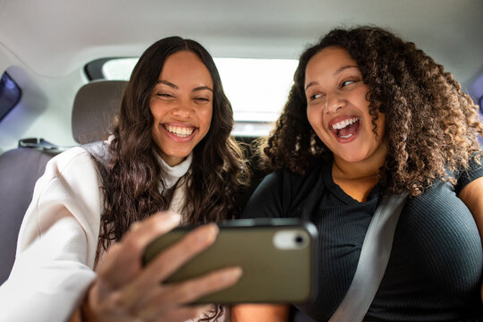 Two Friends Laugh While Holding A Smartphone In the Back Of A Car