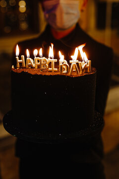 Faceless Waiter Holding Festive Black Cake WIth Candles