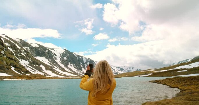 4k video footage of a young woman standing and using her cellphone to photograph the lake in Mre og Romsdal