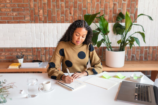 Mixed female taking notes in notepad at office desk