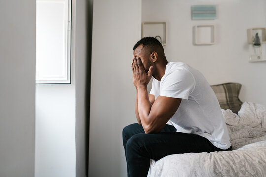 Black man rubbing eyes after awakening in bedroom