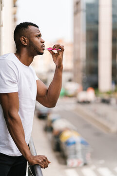 Black guy standing on balcony and brushing teeth