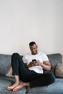 Glad black man browsing social media on sofa