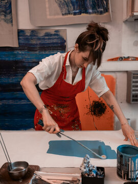 Artist women painting the canvas in deep blue with roller 