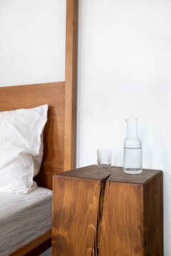 Nightstand with water jug and glass by the wooden bed